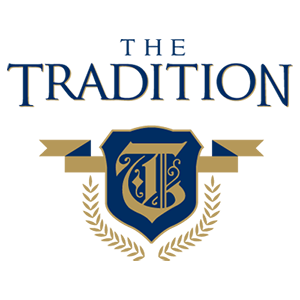 Logo for The Tradition featuring the words in blue, a blue and gold shield with a stylized T, a gold ribbon, and gold laurel branches beneath the shield.